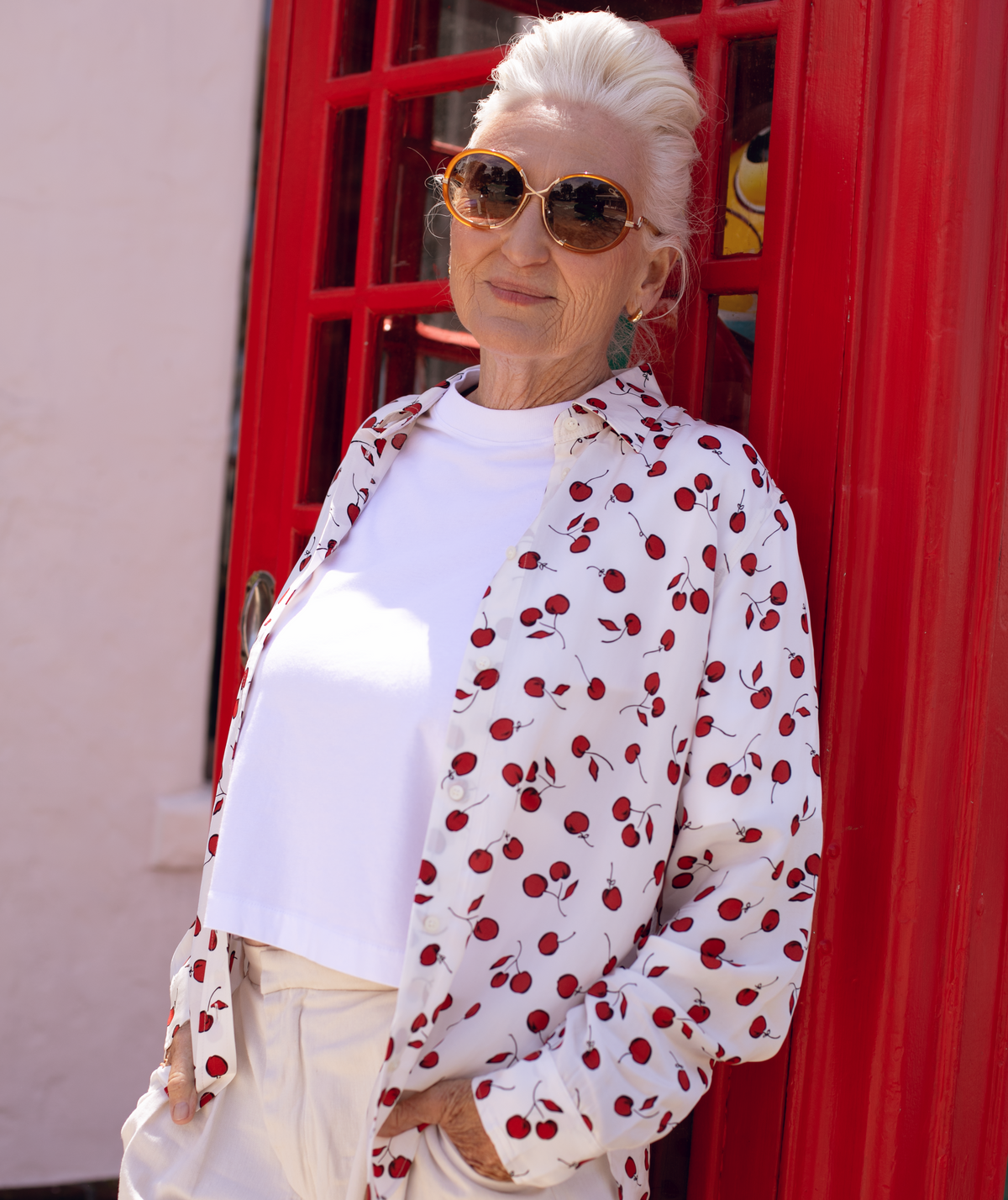Woman wearing sunglasses and a white jacket with red polka dots in front of a red door.